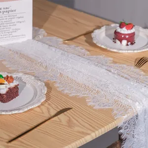 Detail van witte kanten tafelloper met delicate wimperranden op houten tafel