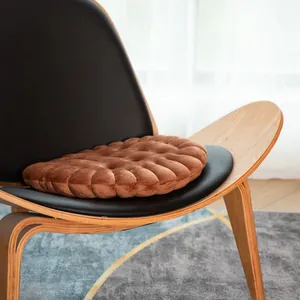 Soft brown biscuit-shaped plush cushion placed on a stylish modern lounge chair