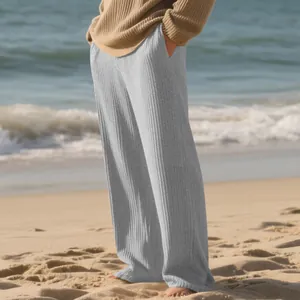 Macro detail of men's grey ribbed wide-leg pants against a coastal beach background.