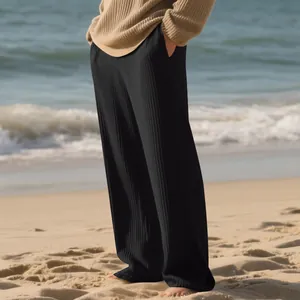 Detailed view of men's black ribbed wide-leg trousers shown in a relaxed beach setting