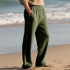 Detailed view of men's olive green ribbed texture wide-leg casual trousers with drawstring at beach.