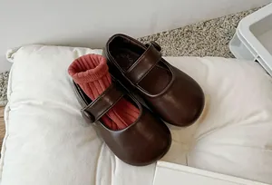 Close-up detail of dark brown children's Mary Jane leather shoes on a white soft pillow