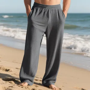 Detailed view of men's grey textured striped wide-leg trousers on a sunny beach
