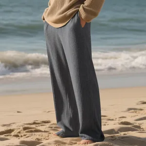 Detail of grey ribbed wide-leg trousers on a beach, showing the soft vertical stripe texture.