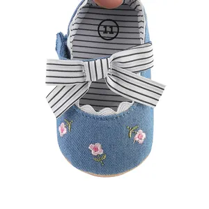 Close-up detail of blue denim baby girl walker shoe with floral embroidery and bow.