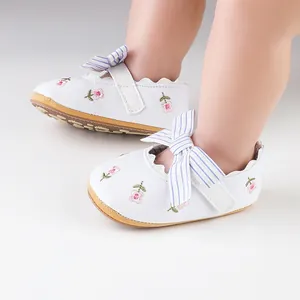 Close-up of white infant girl walking shoes with floral embroidery and striped bow