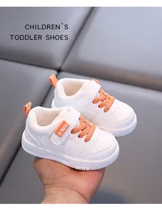 Detail view of white toddler sneakers with orange laces and soft non-slip soles