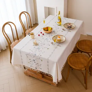Elegant cream tablecloth with blue floral embroidery and tassel fringe in a dining setting.