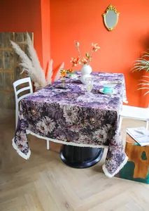 Detail view of purple floral tablecloth with elegant white fringe edges on a dining table.