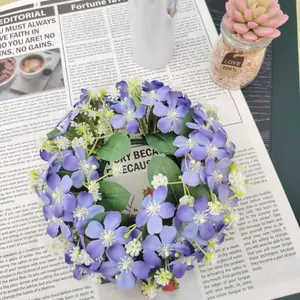 Detail view of an artificial purple flower wreath with green leaves on newspaper.