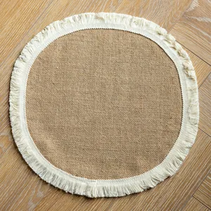 Round farmhouse jute placemat with vintage tassel fringe on a light wood floor background.