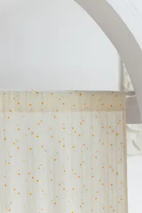Detailed view of cream cotton curtain with delicate white daisy and orange dot pattern.