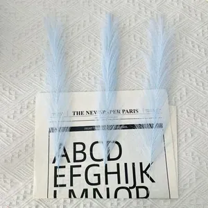 Close-up of three light blue faux pampas grass stems on vintage newspaper background