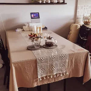 Detail view of vintage beige crochet lace table runner with tassels on a dining table.