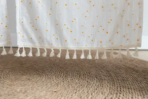 Detail view of a white fabric half curtain featuring orange dots and elegant tassel fringe.