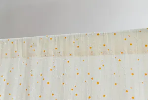 Macro view of white cotton door curtain fabric with yellow daisy floral embroidery.