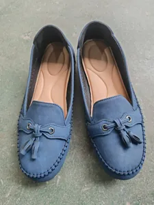 Top view detail of blue suede-style women's loafers featuring decorative tassels.