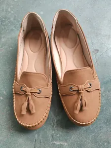 Top-down detail of tan women's loafers featuring tassels and visible stitching.