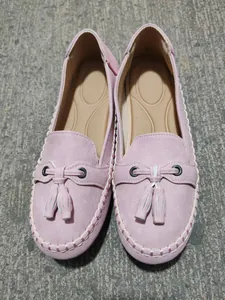 Pink suede women's loafers with tassels and white stitching detail on grey ground.