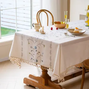 Close-up of elegant beige tablecloth featuring floral embroidery and tassel fringe