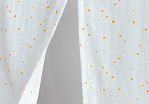 Macro detail of white fabric with vertical stripes and orange daisy floral print.