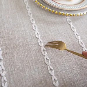 Macro detail showing white embroidered stitching on oatmeal linen tablecloth texture.
