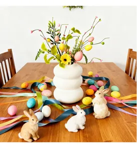 Festliche Oster-Tischdeko mit bunten Eierzweigen in einer weißen Vase und Hasenfiguren