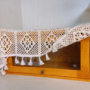 Detail of white vintage crochet lace table runner with tassels on wooden cabinet