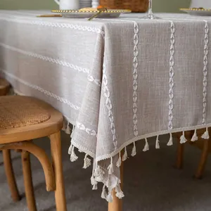 Detail of beige linen tablecloth featuring white stitched patterns and tassel fringe
