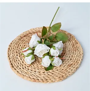 Detailed view of 8-head white artificial rose branch on a woven mat for home decor