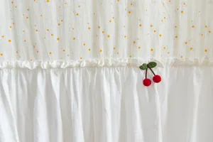 Detailed close-up of white cotton door curtain with daisy patterns and cherry accent
