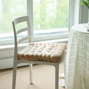 Comfortable soft biscuit-shaped plush chair cushion shown on a white chair in natural sunlight