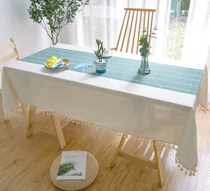 Detailansicht einer weiß-grünen, bestickten Tischdecke mit eleganten Quasten am Rand