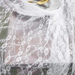 Vue détaillée du motif en dentelle florale blanche sur un tissu de nappe légère.