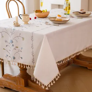 Elegant cream embroidered tablecloth with floral patterns and tassel edges on a wooden dining table