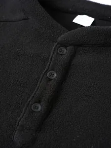 Macro view of a black fleece sweatshirt detailing the Henley collar and resin buttons