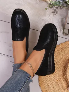 Detail of black shimmering textured slip-on shoes featuring comfortable thick platform soles.