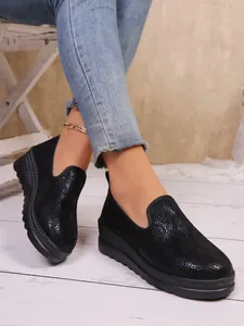 Close-up of black shimmering platform loafers worn with blue jeans and silver anklet