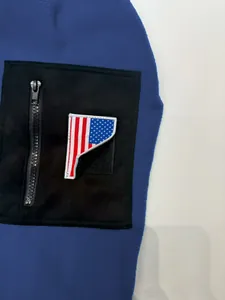 Detailansicht der schwarzen Reißverschlusstasche und der Flagge auf der blauen Fleecejacke.