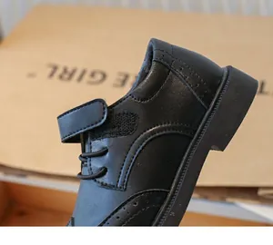 Detailed side view of premium boys black faux leather dress shoes with brogue patterns