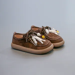 Détail de chaussures rétro en daim marron pour enfants avec cordes et épingles décorées.
