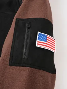 Detail eines braunen Fleecejacken-Ärmels mit schwarzer Tasche und USA-Flaggen-Patch.