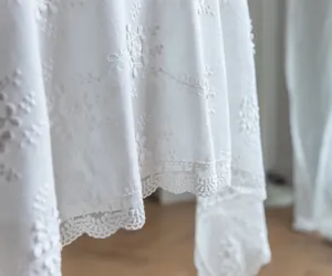Détail d'une nappe en dentelle blanche brodée avec des motifs floraux élégants.