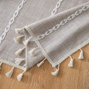 Detailed close-up of a beige linen tablecloth featuring white embroidery and tassels