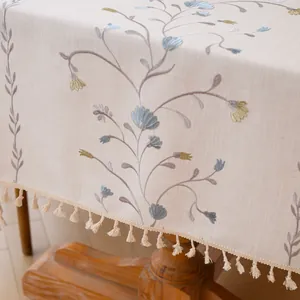 Close-up view of elegant floral embroidery and tassel fringe on a beige linen tablecloth.