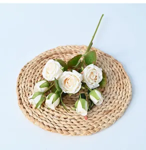 Detailed macro view of 8-head cream artificial roses placed on a rustic woven straw mat.