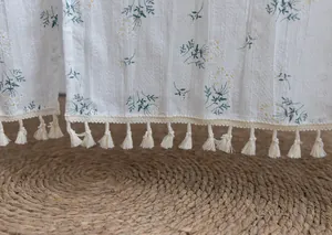 Close-up of white cotton door curtain with floral prints and tassel fringe detail.