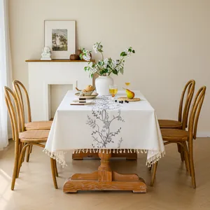 Detailed view of elegant floral embroidery on a cream linen tablecloth with tassels.