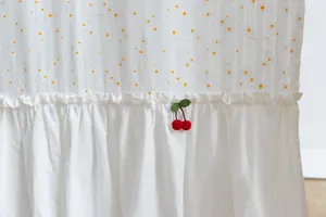 Detail view of artistic white cotton curtain with cute cherry ornament and ruffles.