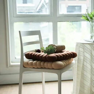 Soft biscuit-shaped plush cushions stacked on a white chair in a sunlit room setting